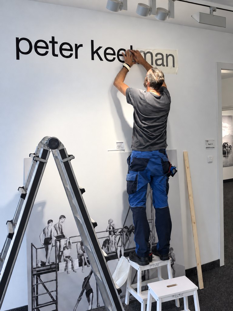 Aufbau der Keetman-Ausstellung: Ein Mann bringt den Schriftzug Peter Keetman an der Wand an.